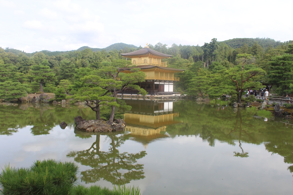 The Golden Temple in Kyoto surrounded by a lake. Reflections of the temple and the trees can be seen in the water.