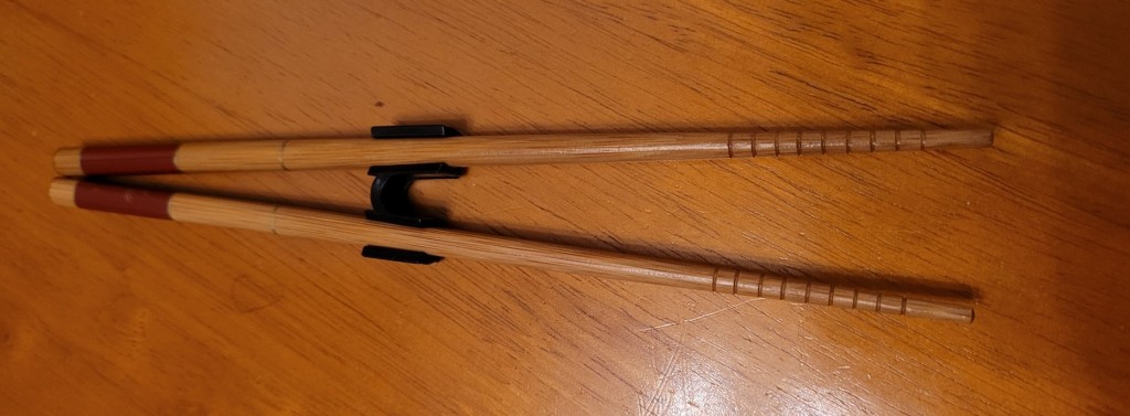 Wooden chopsticks with a black plasticchopstick helper attached.