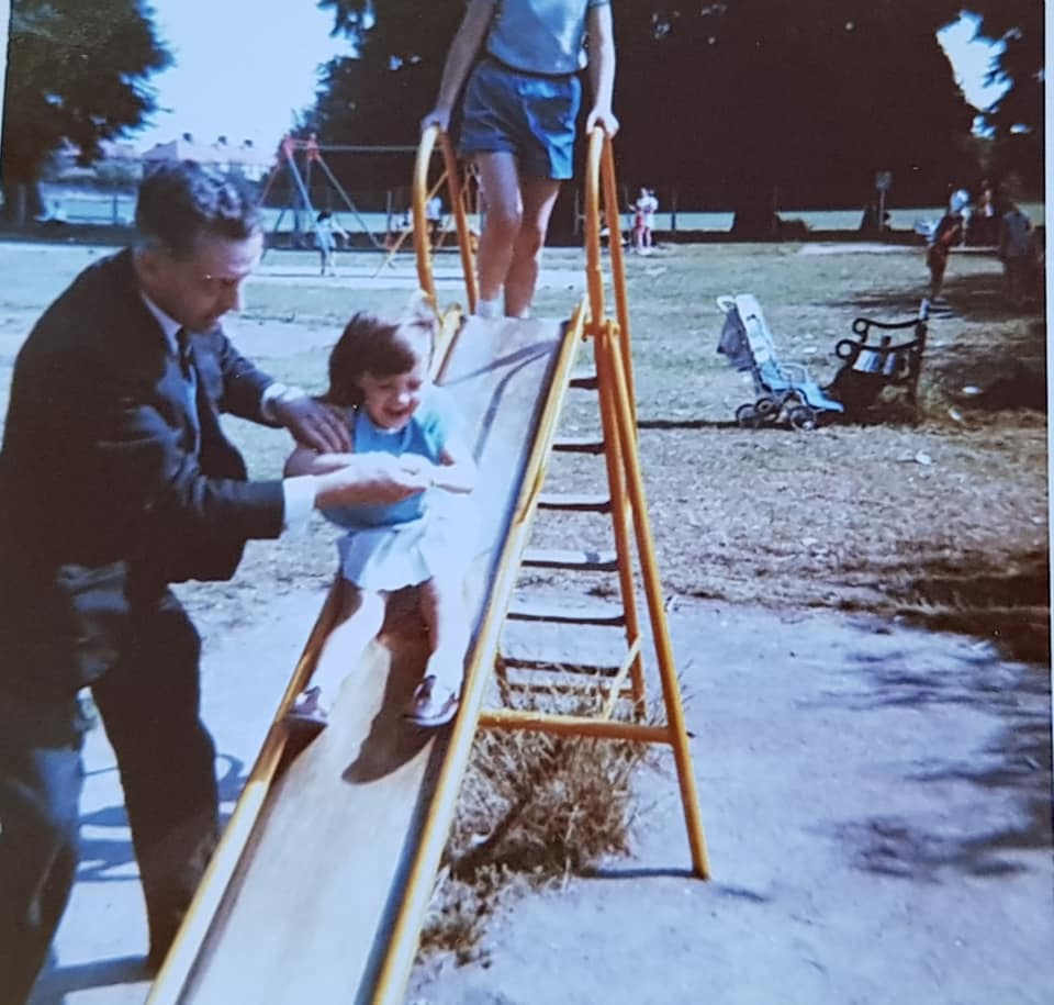 Lynnette as a child going down a slide with her dad helping her.